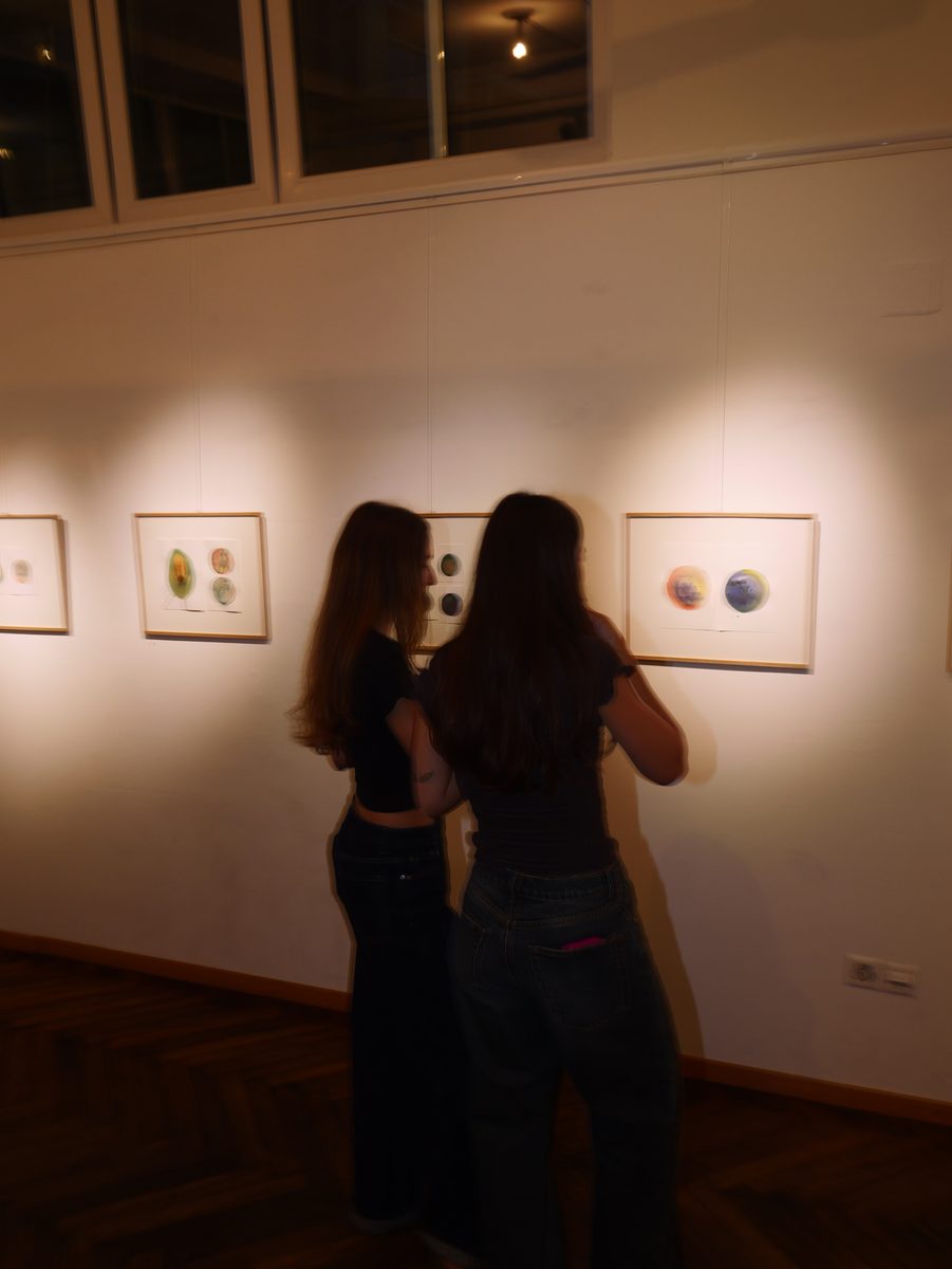 Zwei Besucherinnen von hinten vor beleuchteten Bildern an der Galeriewand