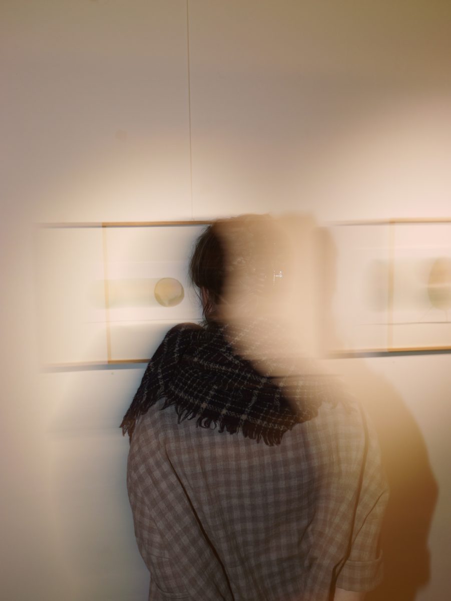 Bewegungsunscharfe Person mit Schal vor einer Reihe gerahmter Bilder